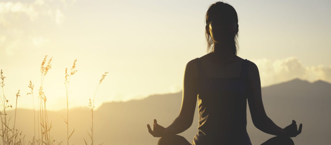 silhouette fitness girl practicing yoga on mountain with sun light